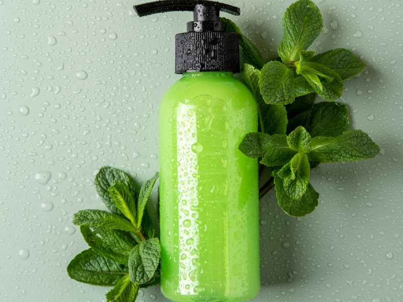 Green cosmetic bottle with dispenser, fresh mint and water drops. Organic cosmetics concept. Cosmetic container mockup with place for text. Natural skincare product.